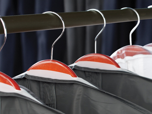 A close-up image of clothing hangers on a rack with garment bags on them