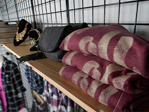 A close up shot of folded shirts and some jewelry displays sitting on a shelf attached to black wire grid