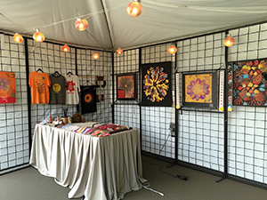 An image of portable wire grid panels set up in a craft show tent displaying orange and brown paintings and merchandise